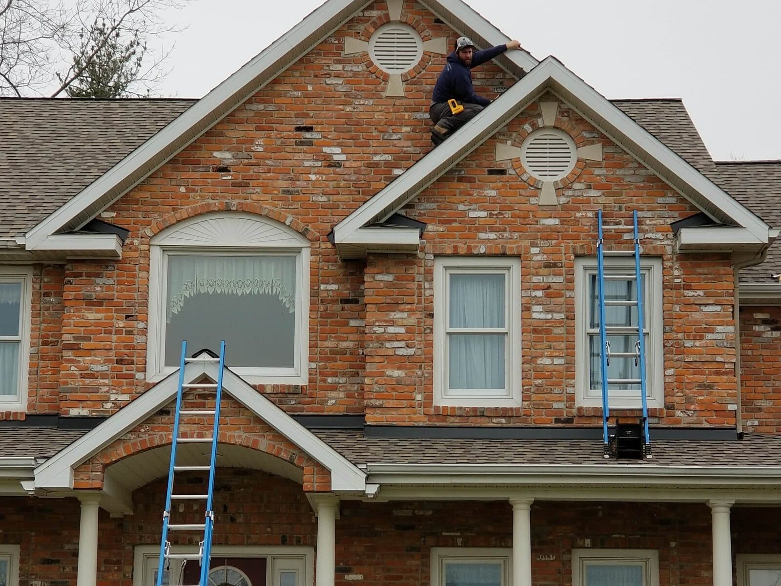 A Voss technician on the roof of a brick home with ladders set against the front