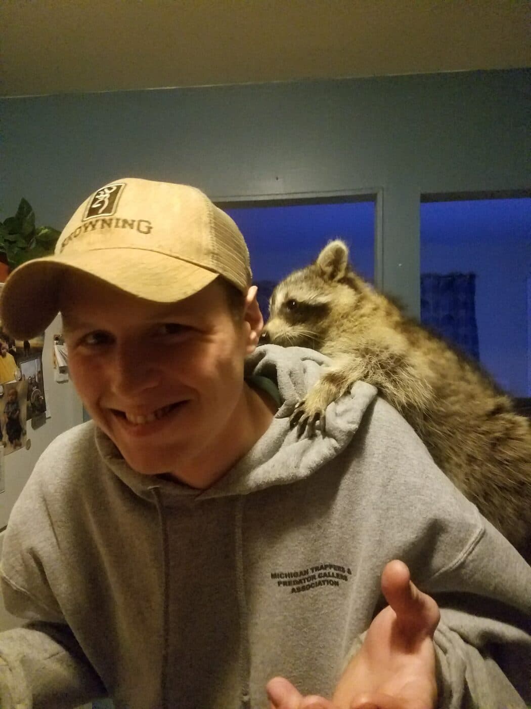 A smiling technician with a young raccoon on his shoulder