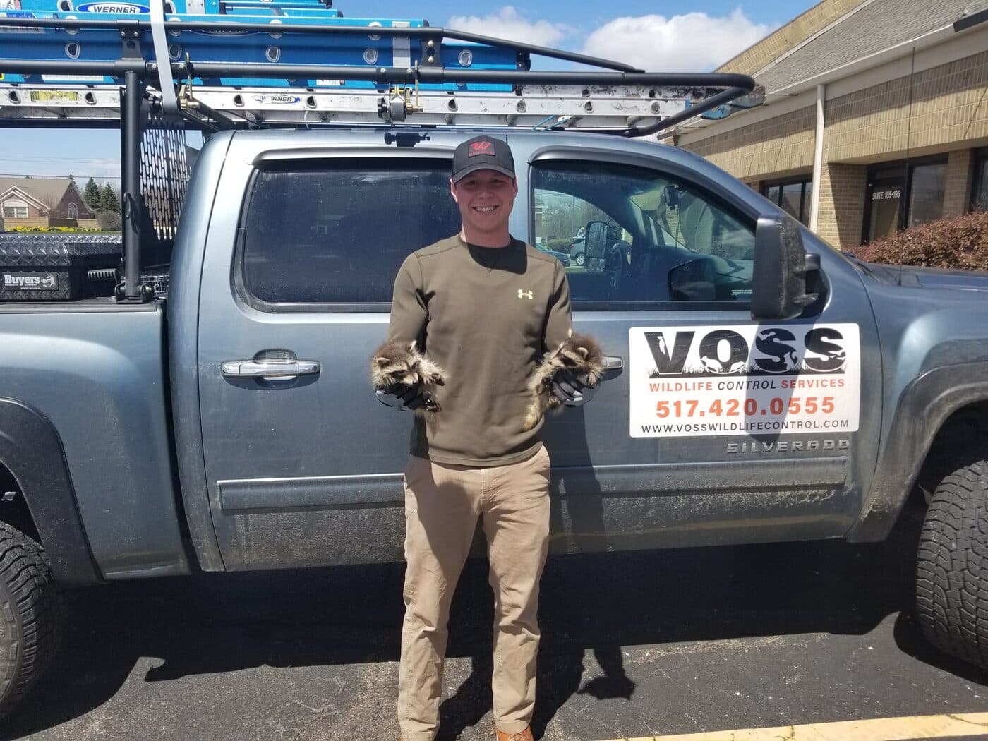 A Voss technician holding two raccoons in front of the company truck
